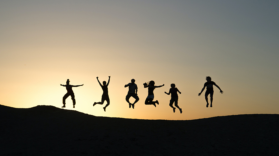 Kuusi ihmistä hyppää ilmaan taustallaan auringonlaskun valo.