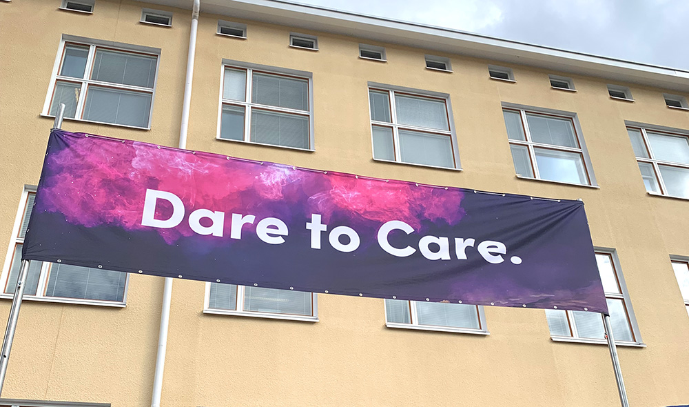 Jyväskylän ammattikorkeakoulun rakennuksen edustalla näkyvä kangaskyltti, jossa teksti Dare to care.