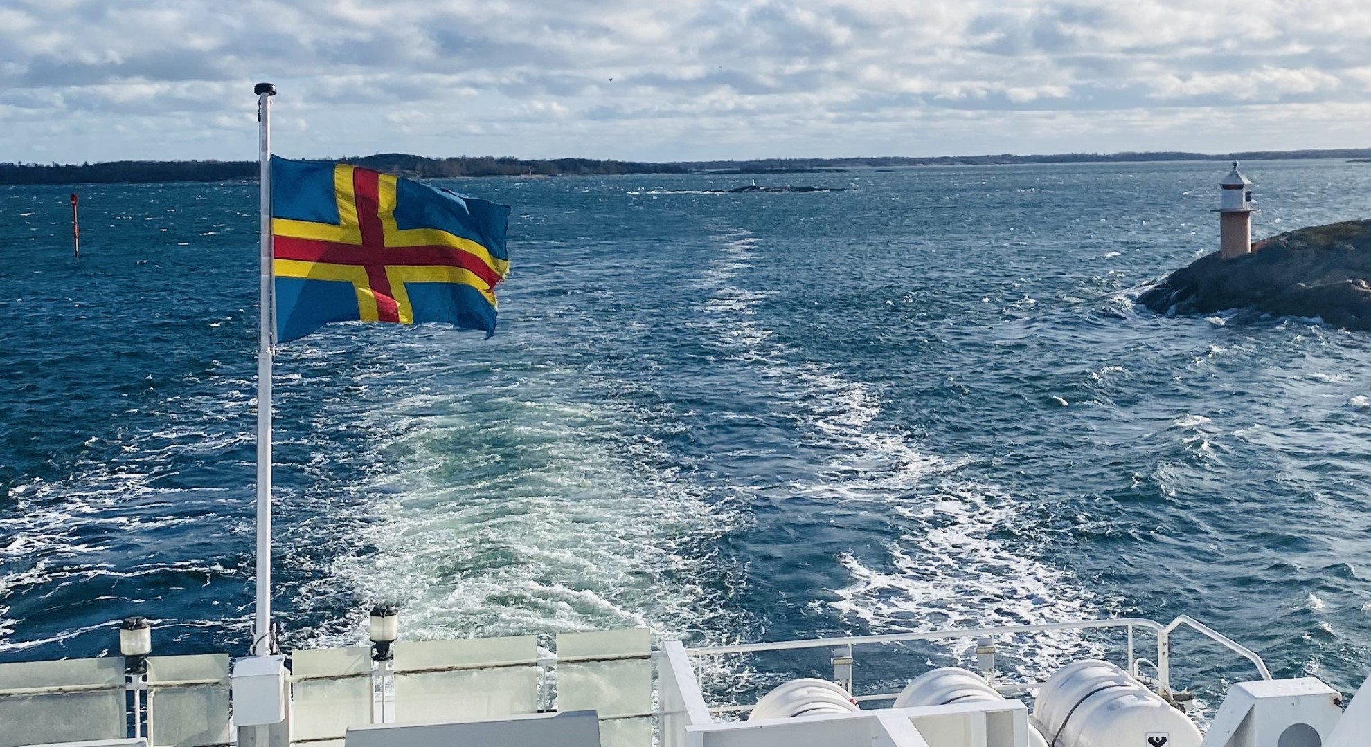 Back of the boat decorated with the Åland flag with a view of the sea behind it
